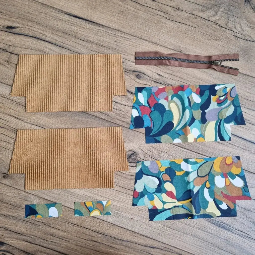 Kit de couture pour trousse d’école en velours côtelé jaune, comprenant deux pièces extérieures, quatre coupons de coton enduit à motif abstrait multicolore, deux petites bandes assorties et une fermeture éclair marron. Disposés à plat sur un sol en bois, ces éléments permettent de créer facilement une trousse d'école zippée originale, pratique et personnalisable, idéale pour un projet DIY ou un cadeau fait main.
