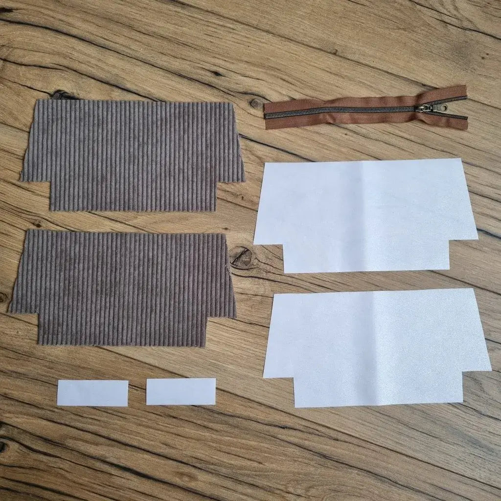 Kit de couture pour trousse d’école en velours côtelé taupe, comprenant deux pièces extérieures, quatre coupons de coton enduit blanc uni pour la doublure, deux petites bandes assorties et une fermeture éclair marron avec zip métallique. Les éléments sont soigneusement disposés sur un sol en bois, prêts à être assemblés pour créer une trousse d'école zippée sobre, élégante et personnalisable, parfaite pour un projet DIY ou un cadeau fait main.