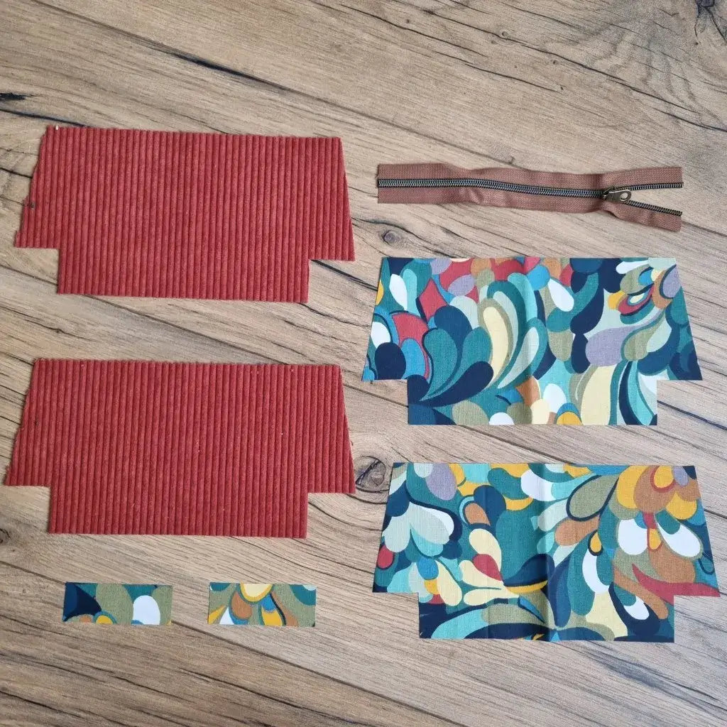Kit DIY pour trousse d’école en velours côtelé terracotta, composé de deux pièces extérieures, quatre coupons en coton enduit à motif abstrait multicolore, deux petites bandes assorties et une fermeture éclair marron. L’ensemble est disposé à plat sur un sol en bois, prêt à être cousu pour réaliser une trousse d'école zippée personnalisée, idéale pour la rentrée ou pour offrir en cadeau fait main.