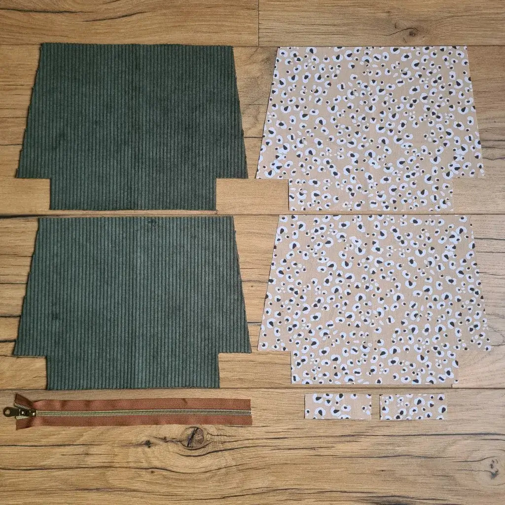 Kit "prêt à coudre" pour une trousse zippée en velours côtelé au coloris vert avec une doublure en tissu à motif léopard. L'ensemble des pièces de tissu, déjà prédécoupées aux bonnes dimensions, sont disposées au sol. A gauche, deux pièces identiques en velours côtelé vert ainsi qu'une fermeture éclair marron. A droite, quatre pièces en tissu imprimé à motif léopard.