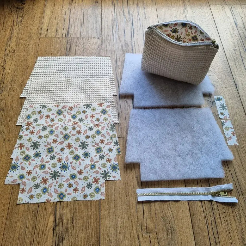 Kit prêt-à-coudre pour trousse zippée matelassée en tissu nid d’abeille écru et coton imprimé floral, comprenant doublure, molleton, fermeture éclair. Idéal pour couture débutant ou cadeau DIY. Un exemple de trousse finie est disposé sur le kit pour illustrer le résultat final.