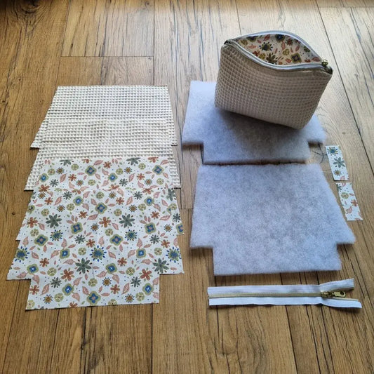 Kit prêt-à-coudre pour trousse zippée matelassée en tissu nid d’abeille écru et coton imprimé floral, comprenant doublure, molleton, fermeture éclair. Idéal pour couture débutant ou cadeau DIY. Un exemple de trousse finie est disposé sur le kit pour illustrer le résultat final.