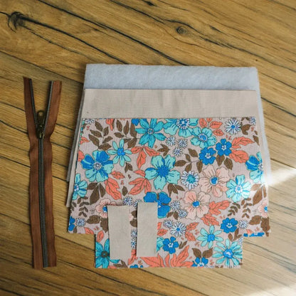 Kit prêt-à-coudre pour fabriquer une trousse zippée en tissu fleuri aux motifs hibiscus dans les tons bleu turquoise, corail et marron. Le kit inclut une fermeture éclair marron avec curseur métallique, des pièces de tissu découpées, une doublure beige et de la ouate pour plus de maintien. Parfait pour un projet DIY couture facile et créatif, idéal pour réaliser une trousse fait main pratique et personnalisée.