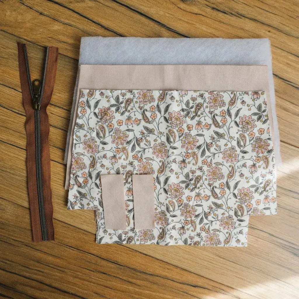 Kit couture DIY pour réaliser une trousse zippée en tissu fleuri motif vintage, avec petites fleurs roses et orangées sur fond clair. Le kit comprend une fermeture éclair marron avec curseur métallique, des pièces de tissu prédécoupées, une doublure beige et des pièces de ouate pour plus de maintien. Idéal pour un projet créatif fait main et pour confectionner une trousse pratique et personnalisée.
