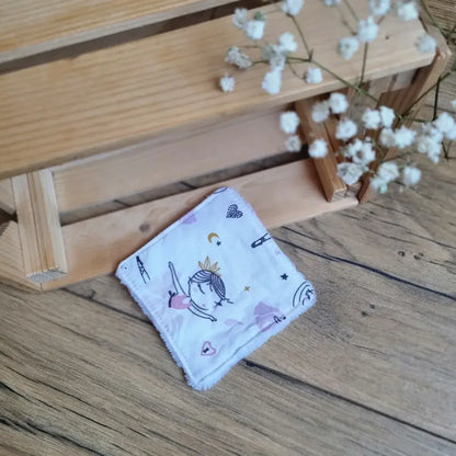 Lingette démaquillante lavable en tissu blanc avec motifs de danseuse, posée sur un sol en bois. Accessoire réutilisable, écologique et zéro déchet, idéal pour une routine beauté respectueuse de l’environnement. Imprimé délicat représentant une danseuse pour une touche de poésie et de douceur. Fabrication artisanale, couture soignée et matière ultra-douce pour un nettoyage du visage tout en confort.