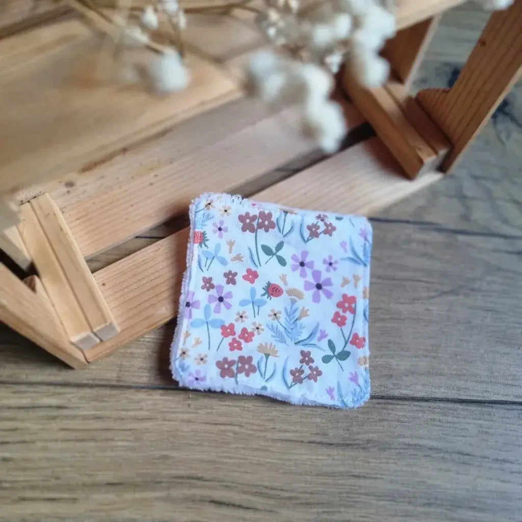 Carré démaquillant réutilisable avec tissu fleuri délicat (fleurs mauves et rouges) et bordure en éponge.