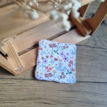 Carré démaquillant réutilisable avec tissu fleuri délicat (fleurs mauves et rouges) et bordure en éponge.