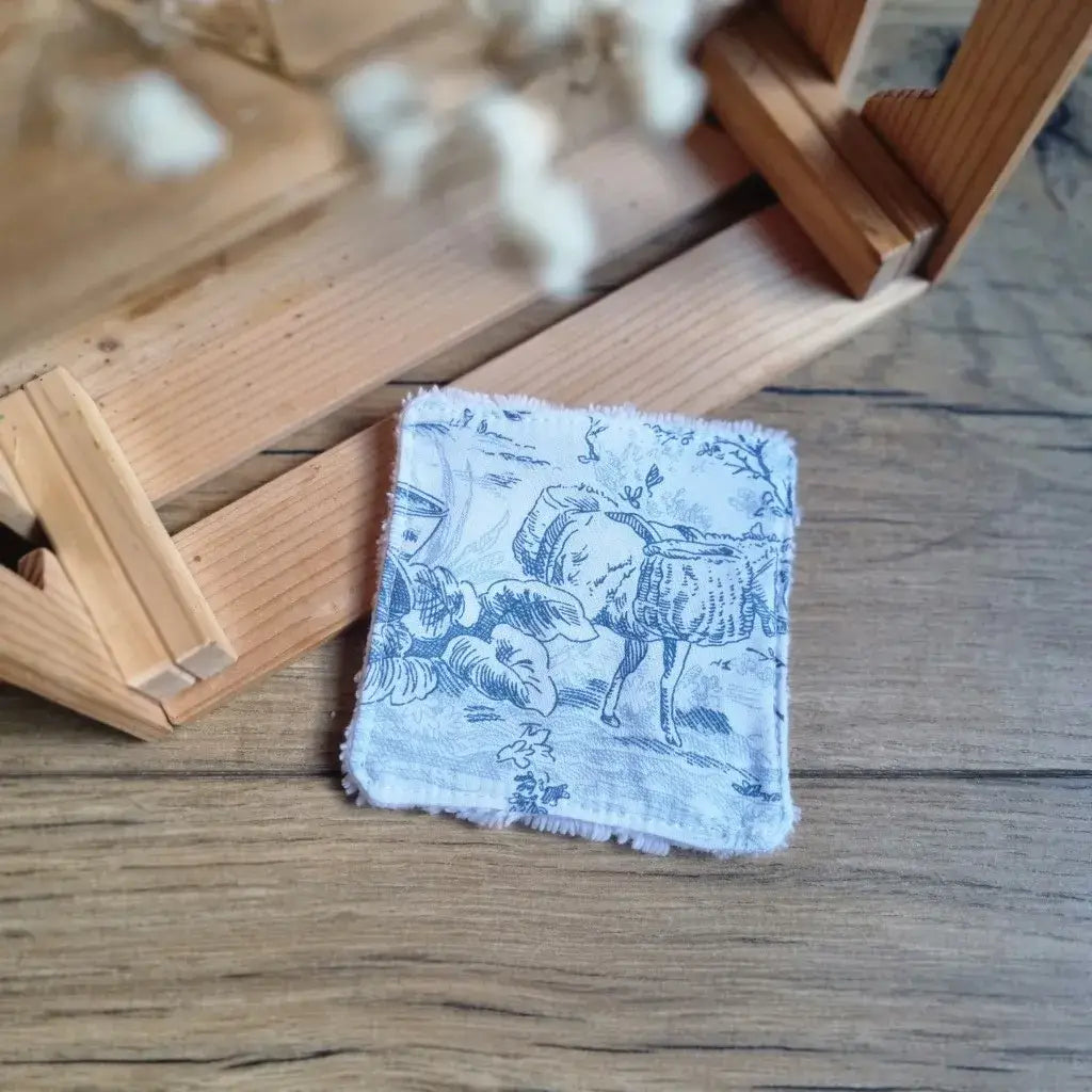 Lingette lavable artisanale en tissu de Jouy bleu et blanc classique, posée devant un décor naturel.