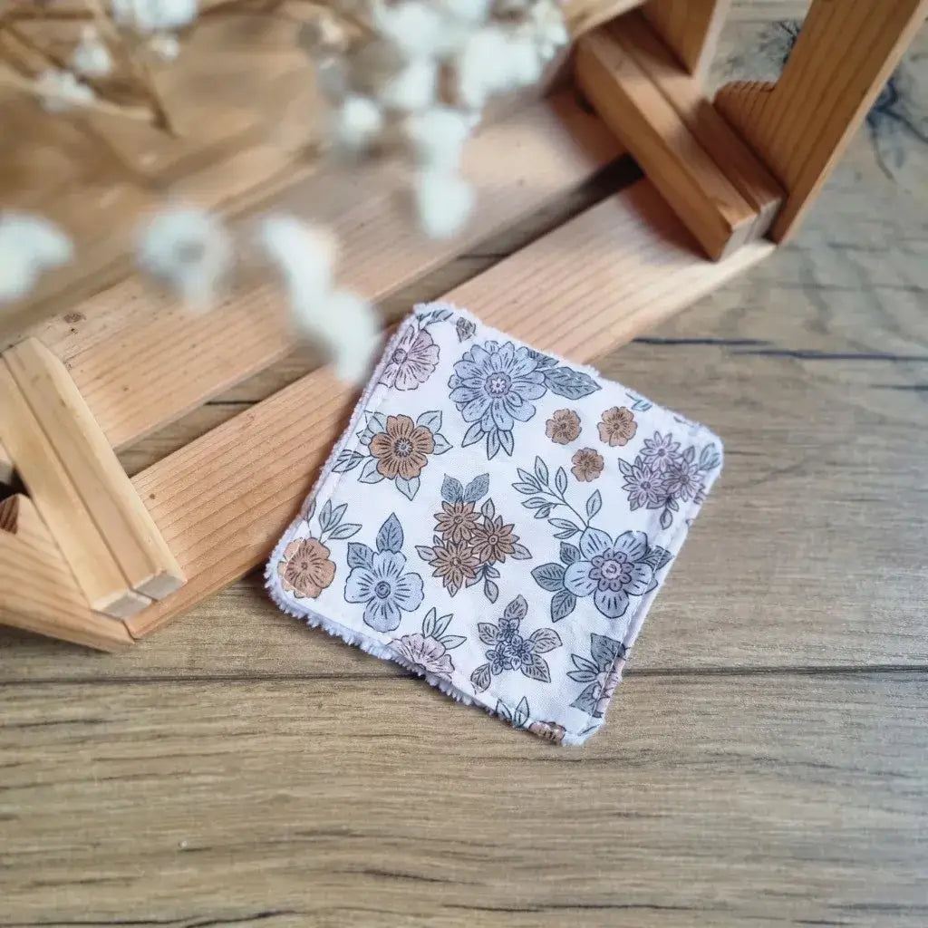 Carré de soin lavable avec imprimé floral bohème dans les tons taupe et bleu ciel sur fond parquet.