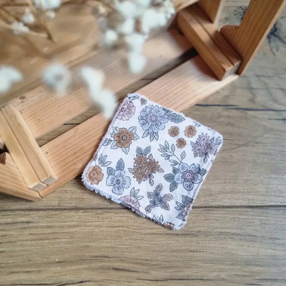 Carré de soin lavable avec imprimé floral bohème dans les tons taupe et bleu ciel sur fond parquet.