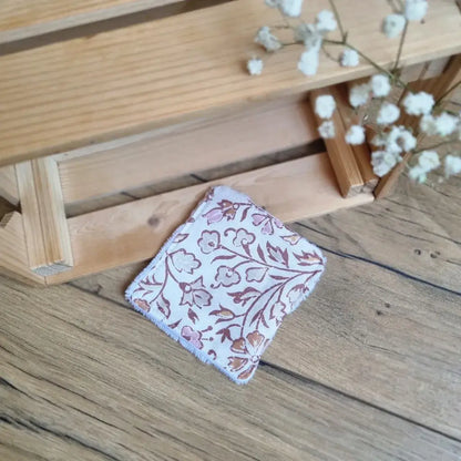 Lingette démaquillante lavable au format maxi 18x18 cm en tissu aux motifs floraux marron sur fond blanc, posée sur un sol en bois. Accessoire de beauté écologique, zéro déchet et réutilisable, idéal pour une routine de soin durable. Design élégant avec imprimé végétal raffiné et typé oriental, couture soignée et texture douce pour un nettoyage du visage en douceur. Fabrication artisanale et respectueuse de l’environnement.