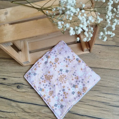 Lingette démaquillante lavable format maxi 18x18 cm en tissu fleuri posée sur un sol en bois. Accessoire zéro déchet, réutilisable et écologique, idéal pour une routine beauté durable. Motif floral délicat sur fond rose, couture soignée et finition douce. Parfait pour un nettoyage du visage tout en douceur. Fabrication artisanale et respectueuse de l’environnement.