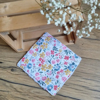 Lingette démaquillante lavable au format maxi 18x18 cm en tissu aux motifs floraux colorés, posée sur un sol en bois. Accessoire de beauté écologique, zéro déchet et réutilisable, idéal pour une routine durable. Motifs fleuris aux teintes vives – jaune, rose et bleu – apportant une touche de fraîcheur et de douceur. Confection artisanale avec des finitions soignées pour un nettoyage du visage tout en respectant la peau et l’environnement.
