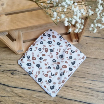 Lingette démaquillante lavable au format maxi 18x18 cm en tissu imprimé léopard, posée sur un sol en bois. Accessoire réutilisable, zéro déchet et écologique, idéal pour une routine beauté responsable. Motif léopard tendance, parfait pour un look sauvage et élégant. Fabrication artisanale avec couture soignée et texture ultra-douce, respectueuse de la peau et de l’environnement