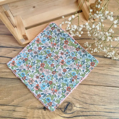 Lingette démaquillante lavable au format maxi 18x18 cm en tissu fleuri, posée sur un sol en bois. Accessoire écologique, réutilisable et zéro déchet, parfait pour une routine beauté durable. Motif floral raffiné aux couleurs vives inspiré des jardins printaniers. Fabrication artisanale avec couture soignée et texture ultra-douce en coton et éponge de bambou, idéale pour un nettoyage du visage tout en douceur et respectueux de l’environnement.