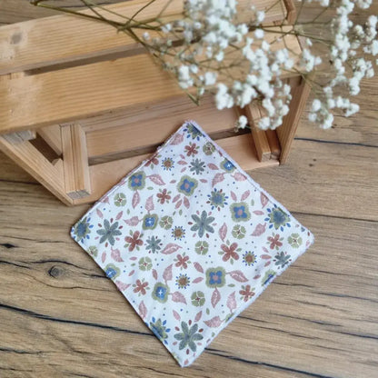 Lingette démaquillante lavable format maxi 18x18 cm en tissu fleuri aux tons verts et marron, posée sur un sol en bois. Accessoire écologique, zéro déchet et réutilisable, parfait pour une routine beauté durable. Motifs floraux délicats inspirés de la nature, couture soignée et douceur au toucher. Idéale pour le nettoyage du visage tout en respectant la peau et l’environnement. Fabrication artisanale et responsable.