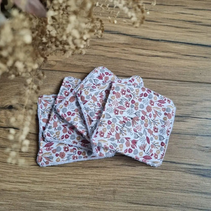 Tas de 5 lingettes en coton lavables et réutilisables au format classique 10x10 cm disposées en éventail sur un parquet en chêne. Ces lingettes présentent une face en coton imprimé d'un motif liberty.