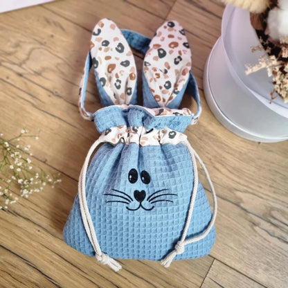 Pochon de Pâques en tissu nid d’abeille bleu denim avec oreilles de lapin motif léopard et cordon de serrage. Flocage d'un visage de lapin sur le devant. Sac personnalisable avec un prénom, idéal pour la chasse aux œufs de Pâques ou comme cadeau unique fait main.