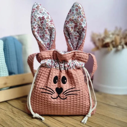 Pochon de Pâques en tissu nid d’abeille coloris marsala avec oreilles de lapin motif liberty et cordon de serrage. Flocage d'un visage de lapin sur le devant. Sac personnalisable avec un prénom, idéal pour la chasse aux œufs de Pâques ou comme cadeau unique fait main.