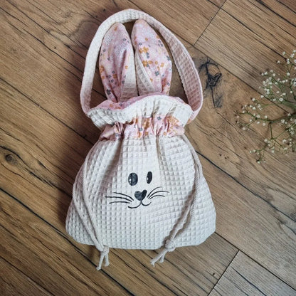 Pochon de Pâques en tissu nid d’abeille coloris naturel avec oreilles de lapin motif bouquet et cordon de serrage. Flocage d'un visage de lapin sur le devant. Sac personnalisable avec un prénom, idéal pour la chasse aux œufs de Pâques ou comme cadeau unique fait main.
