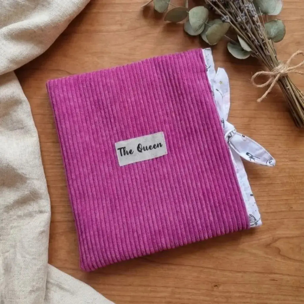 Pochette livre velours côtelé magenta avec étiquette The Queen et intérieur fleuri élégant.