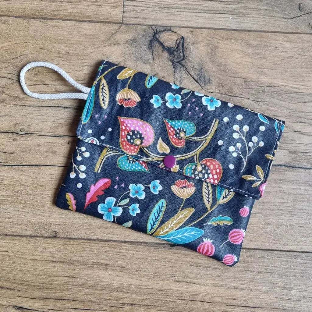 Pochette à savon en coton enduit noir à motif fleurs colorées avec cordon blanc, posée sur du bois.