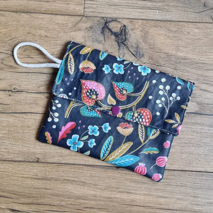Pochette à savon en coton enduit noir à motif fleurs colorées avec cordon blanc, posée sur du bois.