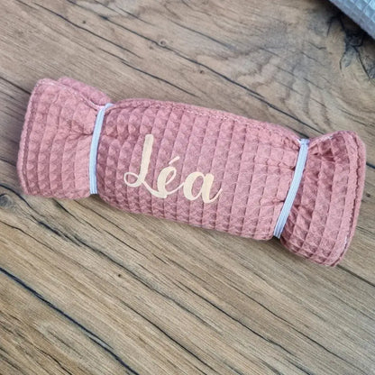 Pochette de rangement multi-usages en nid d'abeille de coloris marsala et personnalisée au prénom de "Léa" floqué en doré. Cette pochette est maintenue roulée grâce à deux petits élastiques à droite et à gauche de celle-ci.