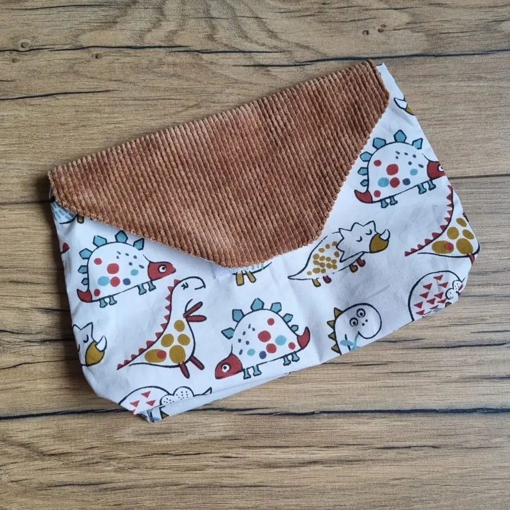 Petite pochette imperméable cousu dans un tissu en coton imprimé au motif dinosaures. La pochette dispose d'un rabat en velours côtelé marron.