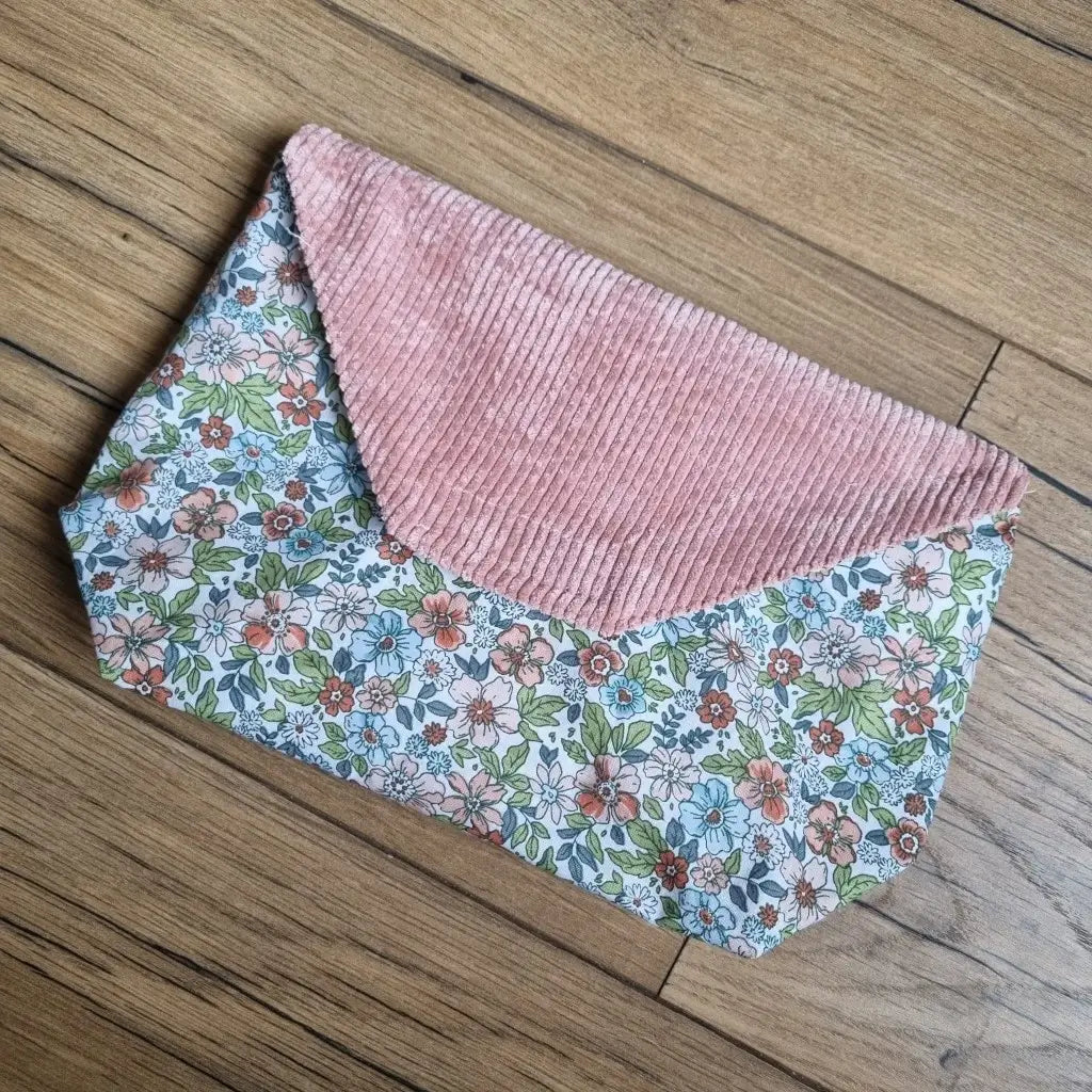 Petite pochette imperméable cousu dans un tissu en coton imprimé au motif fleuri. La pochette dispose d'un rabat en velours côtelé rose.