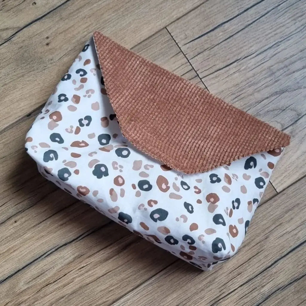 Petite pochette imperméable cousu dans un tissu en coton imprimé au motif léopard. La pochette dispose d'un rabat en velours côtelé marron.