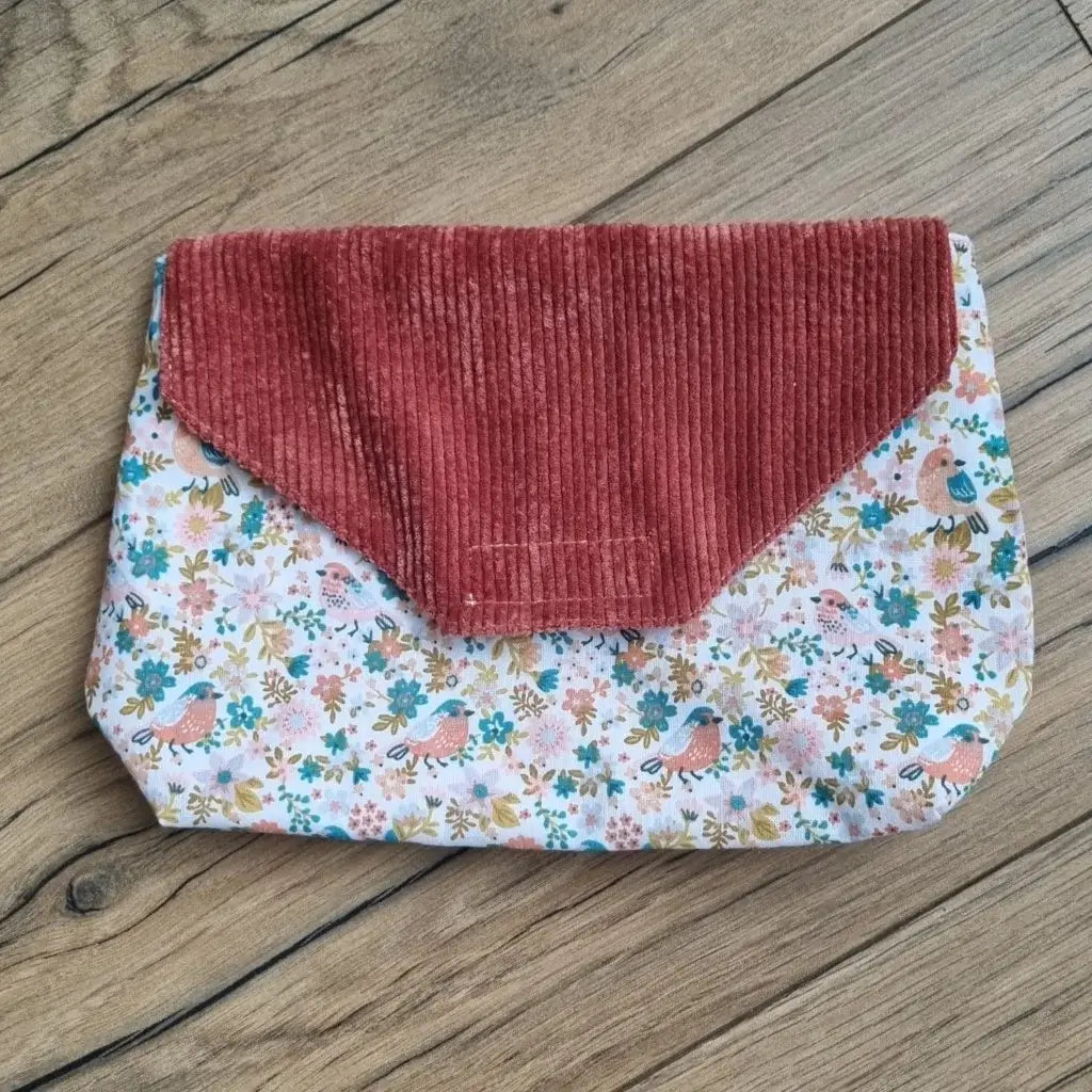 Petite pochette imperméable cousu dans un tissu en coton imprimé au motif oiseaux et fleurs. La pochette dispose d'un rabat en velours côtelé terracotta.