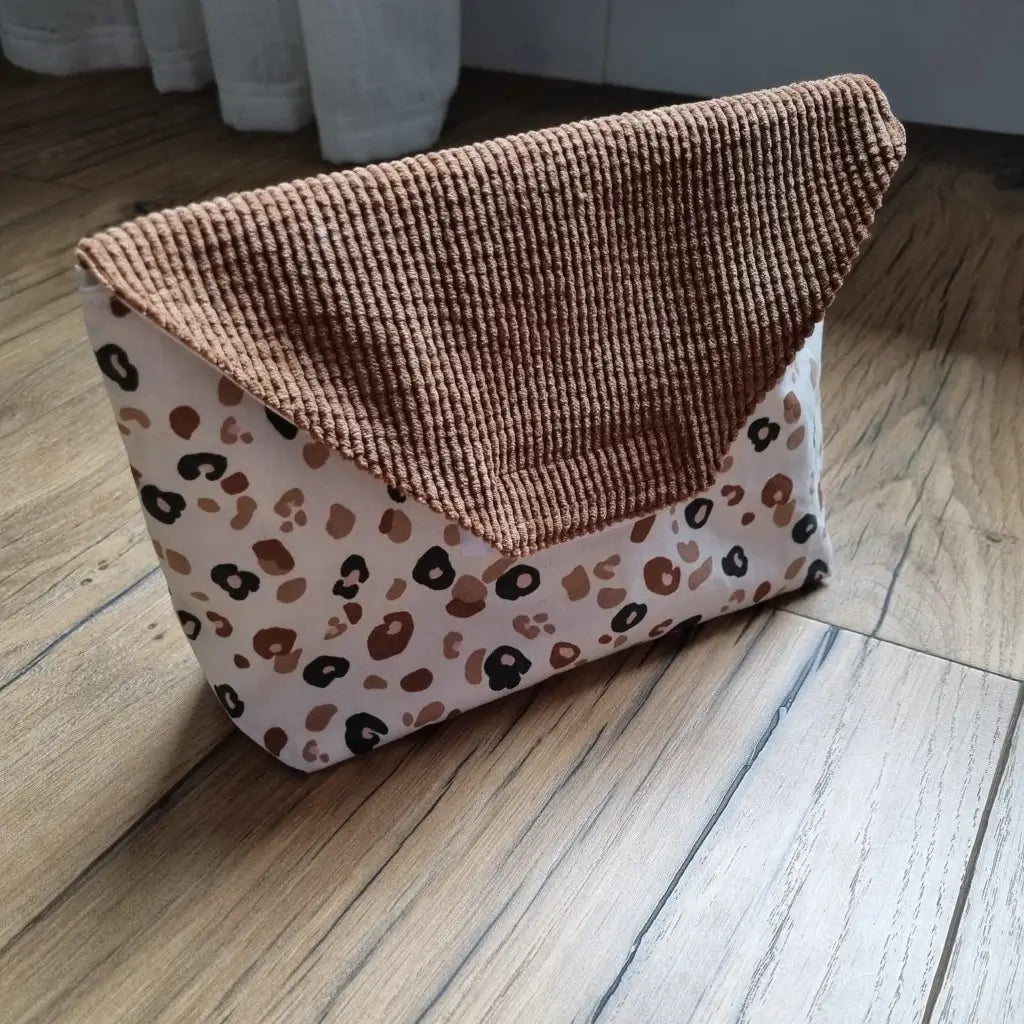 Petite pochette imperméable cousu dans un tissu en coton imprimé au motif léopard. La pochette dispose d'un rabat en velours côtelé marron.