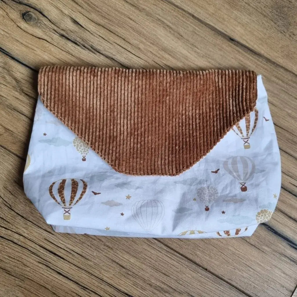 Petite pochette imperméable cousu dans un tissu en coton imprimé au motif montgolfières. La pochette dispose d'un rabat en velours côtelé marron.