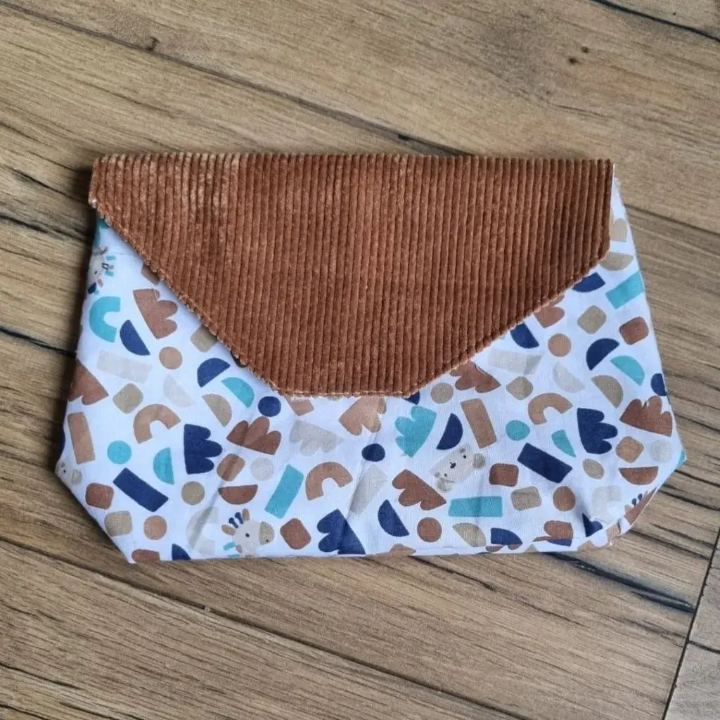 Petite pochette imperméable cousu dans un tissu en coton imprimé au motif ptiwi. La pochette dispose d'un rabat en velours côtelé marron.