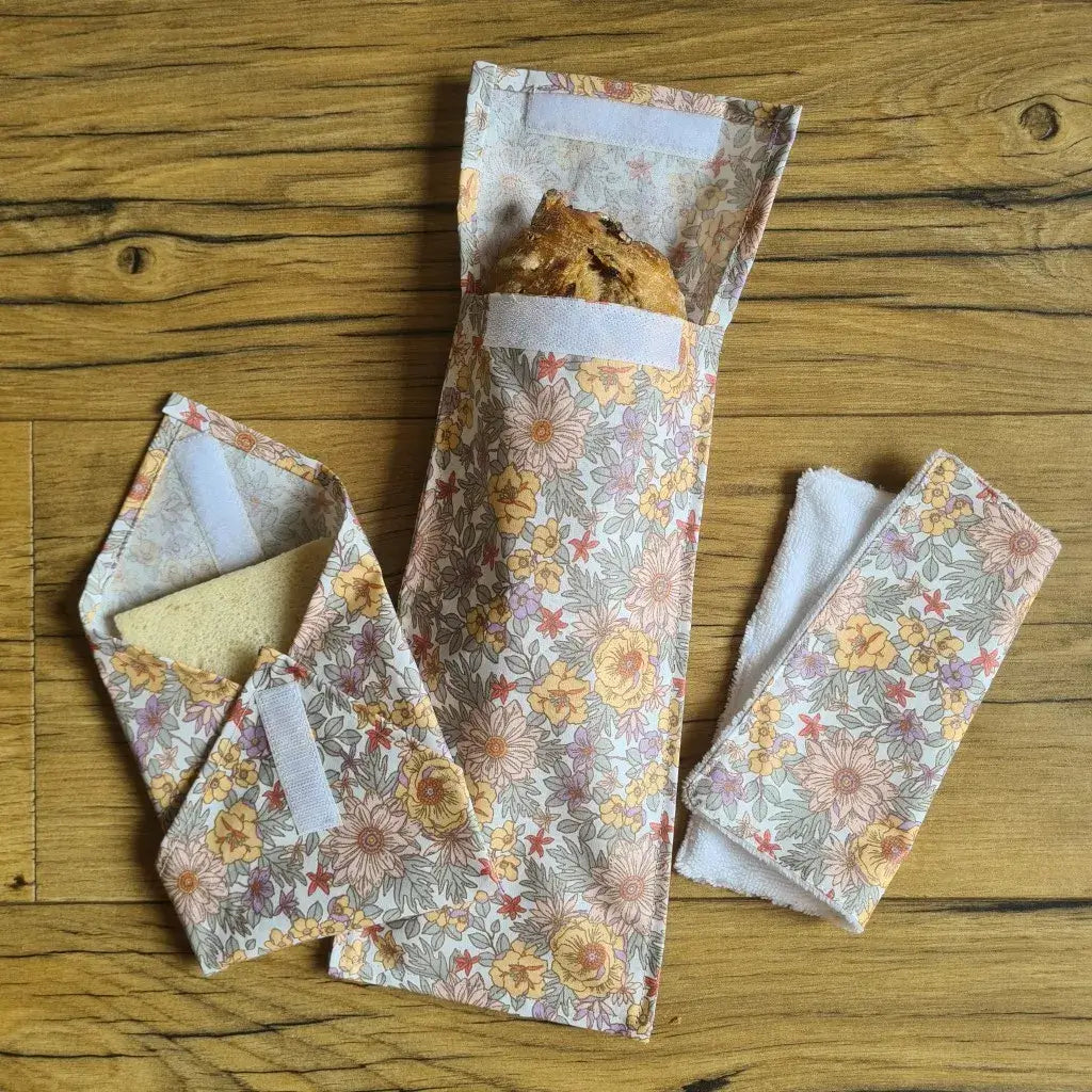 Kit pochettes à sandwichs lavables et réutilisables en coton enduit au motif fleurs mauves comprenant une pochette au format pain de mie, une pochette au format baguette et un essuie-tout lavable avec une face en éponge de bambou blanche.