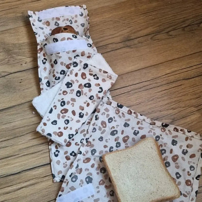 Kit pochettes à sandwichs lavables et réutilisables en coton enduit au motif léopard comprenant une pochette au format pain de mie, une pochette au format baguette et un essuie-tout lavable avec une face en éponge de bambou blanche.
