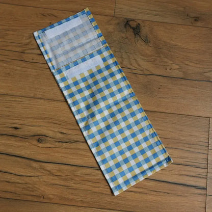 Pochette à sandwich format demi-baguette en tissu enduit à motif carreaux bleus et jaunes, fermée par bande velcro, idéale pour transporter un encas ou un sandwich de manière écologique et réutilisable. Alternative zéro déchet aux emballages jetables pour le déjeuner à l’école ou au bureau.