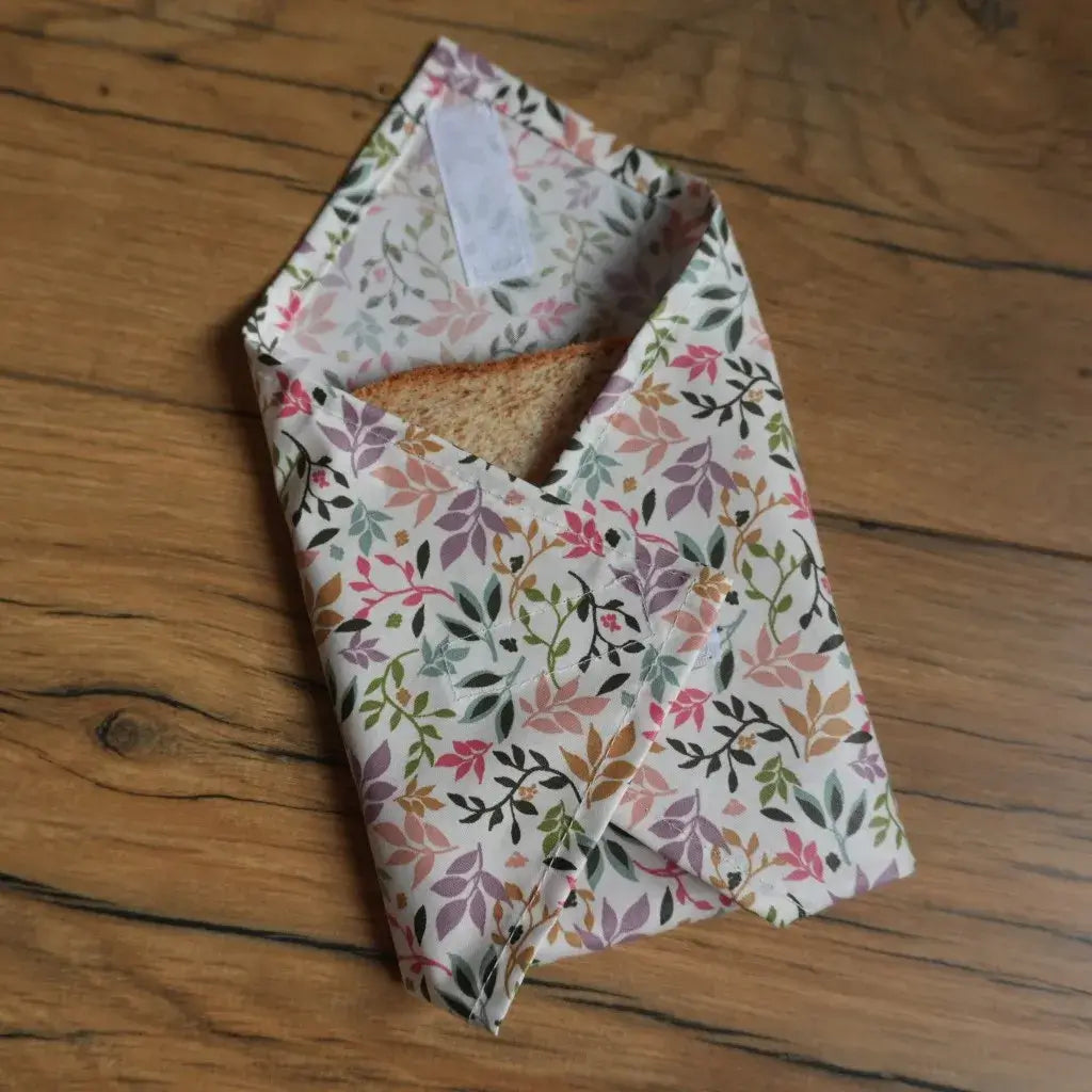 Emballage sandwich lavable en tissu enduit imprimé fleuri, format adapté au pain de mie, avec fermeture velcro pour un maintien sécurisé. Accessoire écoresponsable et pratique pour transporter un encas sans déchet, parfait pour le goûter ou le déjeuner nomade.
