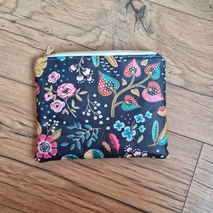 pochette zippée coton enduit bleu nuit avec motif floral coloré posée sur parquet bois