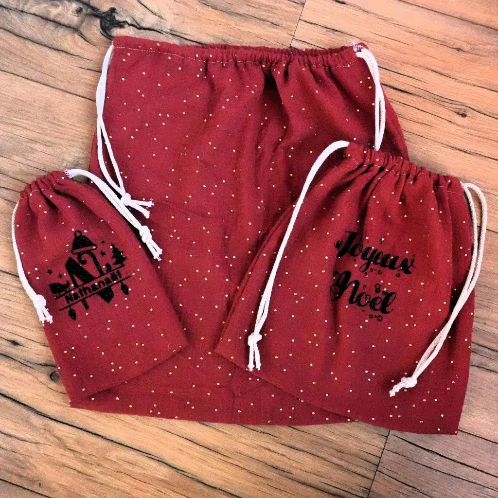 Ensemble de pochons de Noël en double gaze de coton rouge à pois dorés, composé de trois tailles assorties. Le plus petit est personnalisé au prénom “Nathanaël” avec un motif noir festif, tandis que le moyen affiche l’inscription “Joyeux Noël”. Réalisés à la main, ces pochons à cordon allient charme artisanal et esprit de fête pour un emballage cadeau réutilisable, chic et écologique sous le sapin.