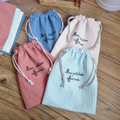 Lot de pochons en tissu nid d’abeille doublés et personnalisés avec l’inscription floquée 'Mes petites affaires', disponibles en plusieurs coloris : bleu denim, menthe, naturel et marsala. Sacs de rangement en coton lavable, pratiques pour les affaires de bébé, les jouets ou les accessoires du quotidien.