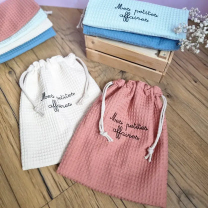 Pochons personnalisés en tissu nid d’abeille doublés, floqués avec l’inscription 'Mes petites affaires', coloris naturel, marsala, menthe et bleu. Sacs de rangement écoresponsables pour bébé ou enfant, parfaits pour organiser les petites affaires dans une valise, un sac à langer ou à la maison.