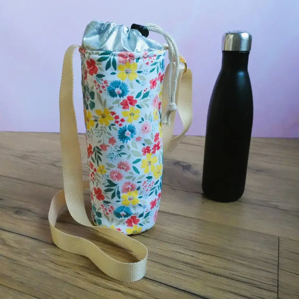 Porte-gourde isotherme en coton enduit motif floral Bridget avec fleurs rouges, jaunes et bandoulière beige.
