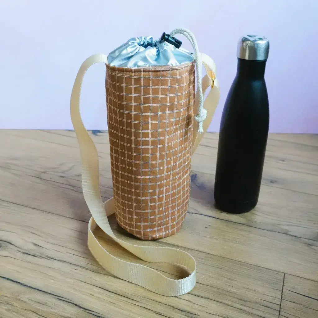 Porte-gourde isotherme en coton enduit à motif carreaux terracotta, avec bandoulière beige et intérieur isolant argenté.