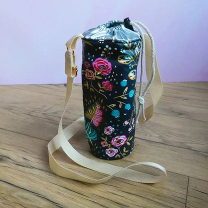 Sac à gourde isotherme motif nuit fleurie avec fleurs roses et baies turquoise sur fond noir, bandoulière beige.