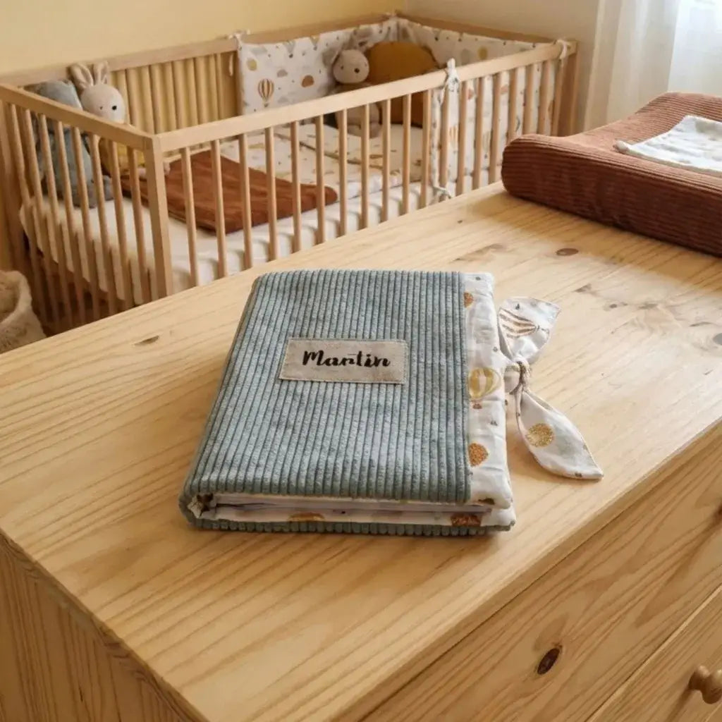 protège carnet de santé bébé velours côtelé vert lichen avec lien tissu posé sur table chambre enfant