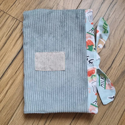 Protège carnet de santé en velours côtelé de coloris bleu clair. Ce protège carnet de santé se ferme à l'aide d'un ruban en tissu imprimé au motif kawai. Il est personnalisable avec le prénom de l'enfant floqué sur une petite étiquette en tissu.
