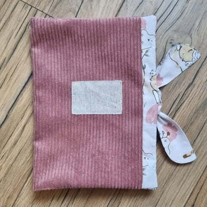 Protège carnet de santé en velours côtelé de coloris rose. Ce protège carnet de santé se ferme à l'aide d'un ruban en tissu imprimé au motif danseuse. Il est personnalisable avec le prénom de l'enfant floqué sur une petite étiquette en tissu.