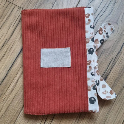 Protège carnet de santé en velours côtelé de coloris terracotta. Ce protège carnet de santé se ferme à l'aide d'un ruban en tissu imprimé au motif léopard. Il est personnalisable avec le prénom de l'enfant floqué sur une petite étiquette en tissu.